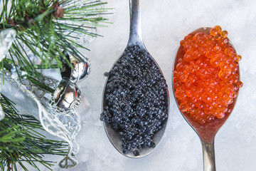 Christmas food concept: two spoons with black caviar and red salmon roe on snow background. Close...