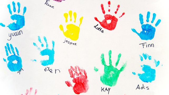 Bunte Handabdrücke von Kinderhänden auf weisser Wand mit Namen