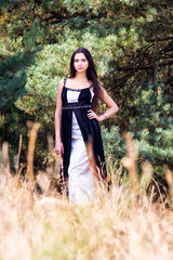 Graceful charming brunette model posing in black dress in coniferous park