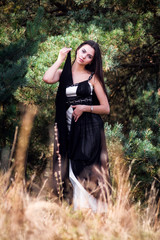 Graceful charming brunette model posing in black dress in coniferous park
