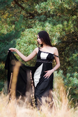 Naklejka premium Graceful charming brunette model posing in black dress in coniferous park