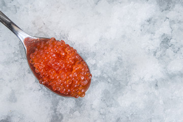 Spoon with salmon roe on snow background. Top view, with copy space