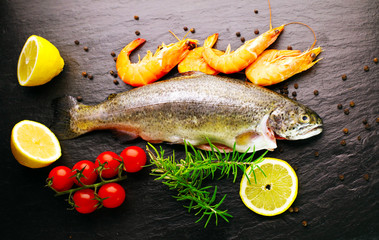 Delicious fresh fish on dark vintage background. Fish with aromatic herbs, spices and vegetables - healthy food, diet or cooking concept