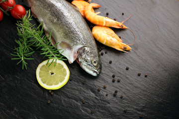 Delicious fresh fish on dark vintage background. Fish with aromatic herbs, spices and vegetables - healthy food, diet or cooking concept