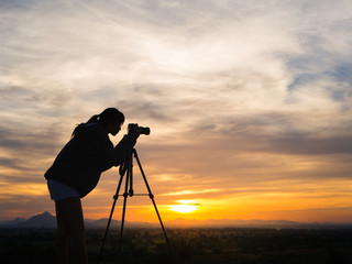 Silhouette of woman shooting with camera at sunset