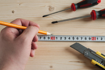 Hand with pencil, measuring tape and other tools