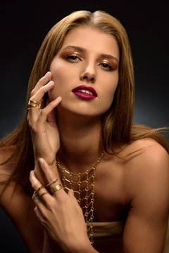 Fashion photo of attractive young blonde woman with styled make–up, long necklace and many rings on her fingers