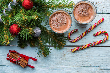 Two glasses of cocoa and christmas tree with toys on white wooden background.