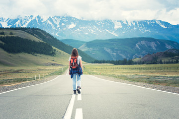 Lonely girl with a backpack walking along the road. In the distance, mountains. Altai, Russia.