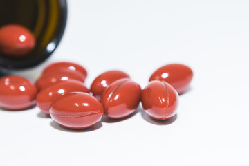 Red vitamin capsule from the bottle on white background