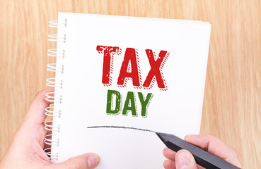 Tax day word on white ring binder notebook with hand holding pen