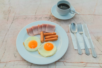 Breakfast with Fried egg, Ham, Sausage and black coffee on marble table.
