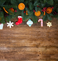 christmas gingerbread frosted cookies with fresh fir tree, berries and oranges, copy space on aged wooden background