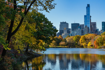 Fototapeta na wymiar Fall in Central Park at The Lake with Midtown skyscrapers. Cityscape sunrise view with colorful Autumn foliage. Manhattan, New York City