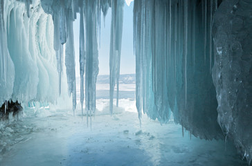 Long  blue icicles in the ice cave at coastal cliffs. Unusual natural phenomena of winter Lake...