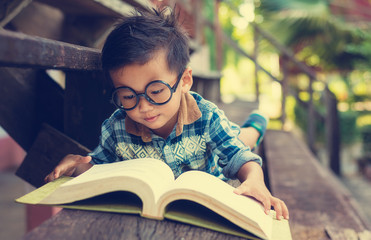 Little boy reading a book on the wooden floor