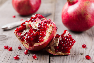 Whole and broken red ripe juicy pomegranates on rustic wooden unpainted table