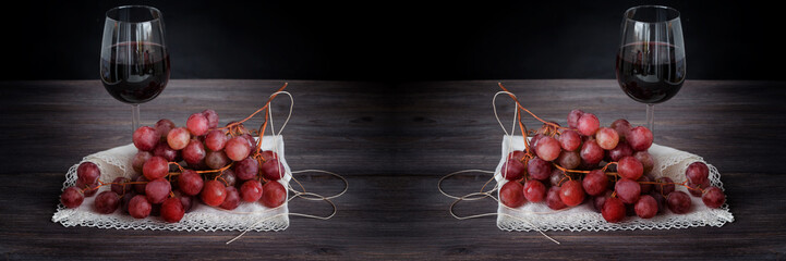 Red wine in wine glass and bunch of dark red grapes on wooden board against black background. Toned image. Copy space. Wide panoramic.