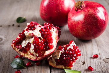 Whole and broken red ripe juicy pomegranates on rustic wooden unpainted table