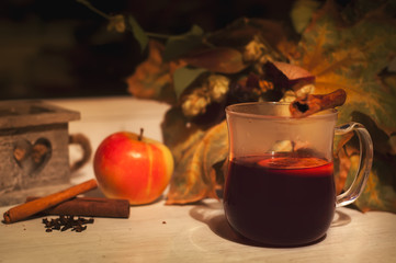 Glass of hot mulled wine on wooden table with candle, apple and cinnamon