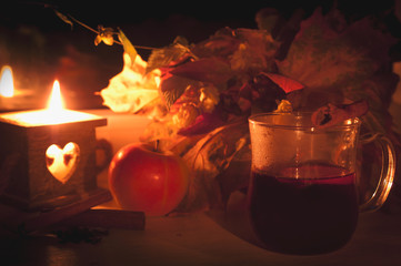 Glass of hot mulled wine on wooden table with candle, apple and cinnamon