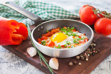 fried eggs with a tomato and a paprika in a frying pan on a board, selective focus