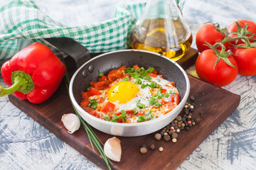 fried eggs with a tomato and a paprika in a frying pan on a board, selective focus