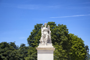 Obraz premium View of winged woman statue at Jardin Des Tuileries in Paris. Trees and blue sky are in the background.