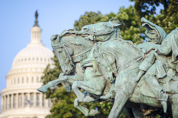 Bronze memorial of horses (Artillery, 1912) charging forward with the US Capitol Building dome under blue sky in the background in Washington, DC