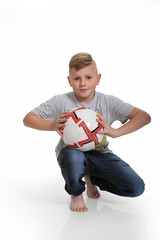 Śliczny chłopiec, blondyn stoi z piłką na białym tle.