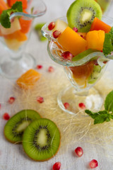 Fruit desserts, salad of pineapple, papaya, pomegranate and mint, kiwi on light background