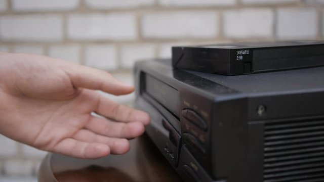 Close up of a VHS tape being ejected from a VCR. Black vintage video tape player.