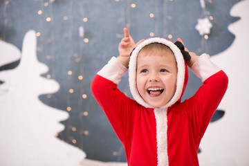 Очень веселый ребенок в рождественском костюме на новогоднем фоне - obrazy, fototapety, plakaty