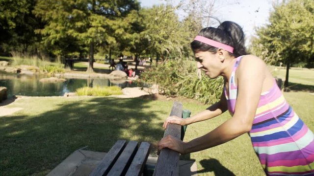  young woman doing pushup off the back of a park bench experiences pain in her wrist.