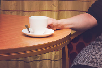 Recreation at the table with a cup of coffee in a cozy atmosphere in the room. Coffee break. Hand holding a white cup.