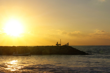 Obraz premium Silhouettes of fishermen at sunset. Rocky shore for fishing. Evening sky and quiet sea background.