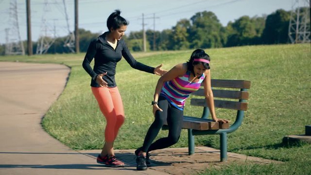 One of the two sisters out for a morning jog pulls a hamstring muscle and limps to a nearby bench while other sister shows great concern.