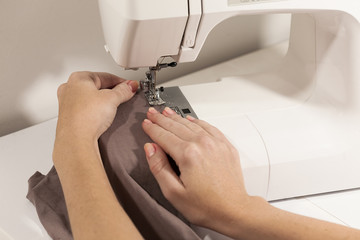 Hands sewing on white sewing machine brown fabric