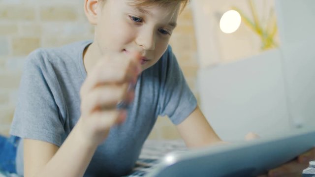 The boy lies on a sofa and watches the movie on the tablet