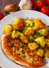 Grilled chicken breast with potato in a plate on wooden table. top view