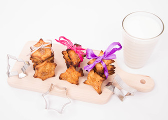 Christmas cookies and cookie cutters on a wooden board with a glass of milk on a white background