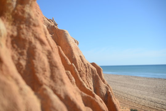 Closeup on red rock wall with defocused beach and sea. Sunny outdoors background