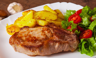 grilled meat fillet steak with fried potato and vegetables salad in a plate on wooden table