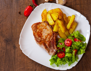 grilled meat fillet steak with fried potato and vegetables salad in a plate on wooden table