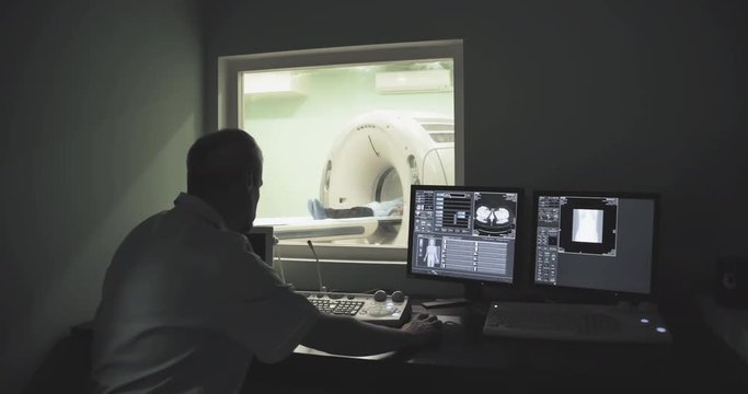 Doctor looking at computer screen while patient in CT MRI scanner 4k video. Computed tomography imaging on monitor