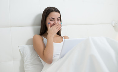 Woman using tablet in light room. She lies on bed and laugh.