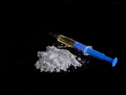 Cocaine drug powder pile and injection syringe on black background