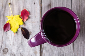 Cup of coffee surounded by red, purple and yellow fall leaves
