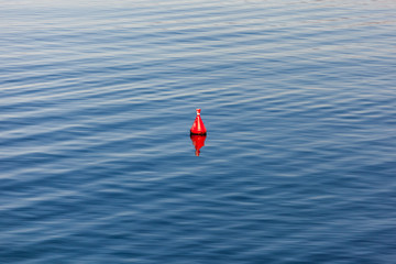 Red buoy with mirror image floating in blue ocean with wave pattern