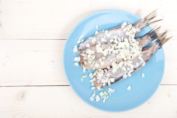 Traditional Dutch raw herring with onions on plate on wooden background